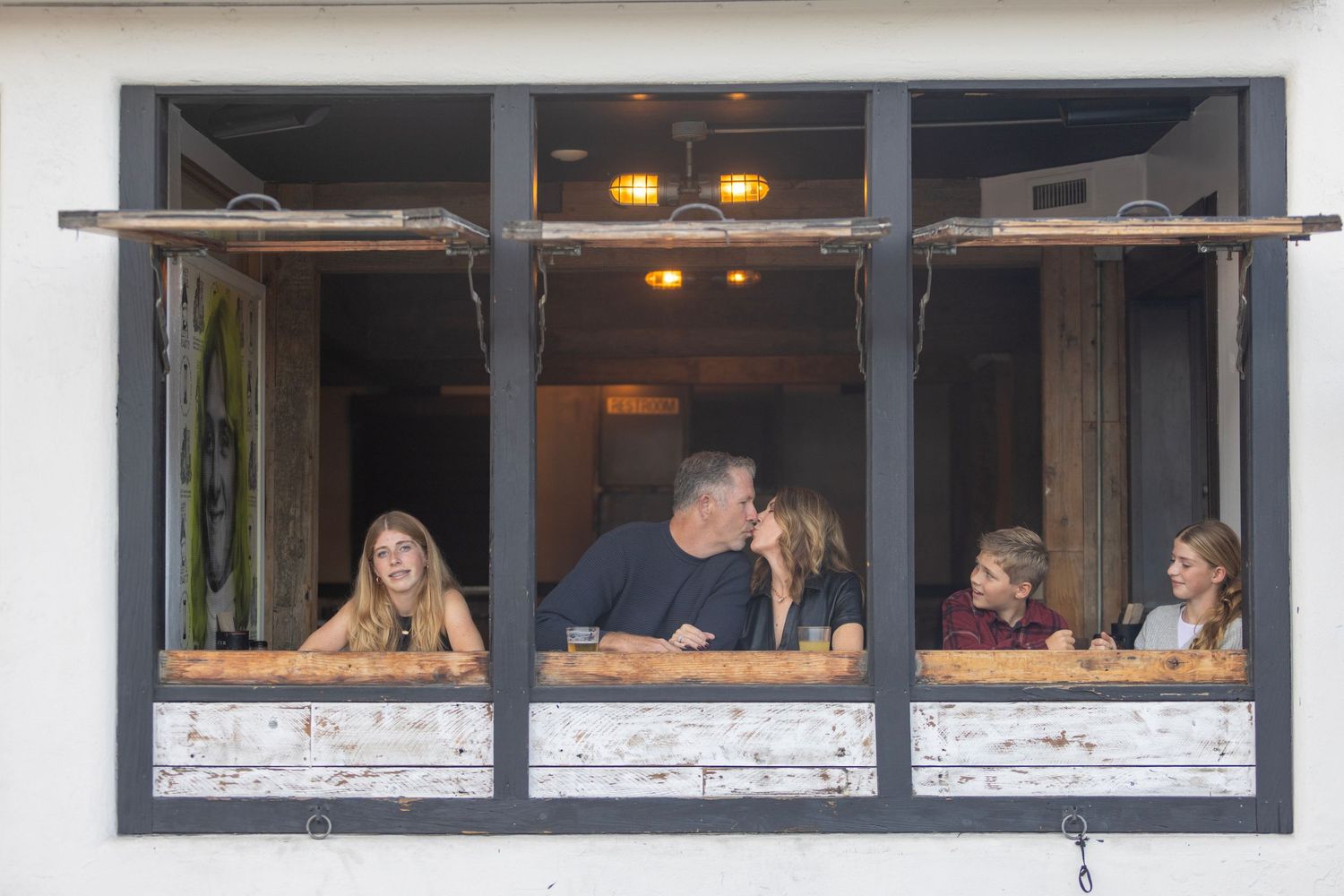Family of five smiling and leaning on a rustic window ledge inside a cozy restaurant.