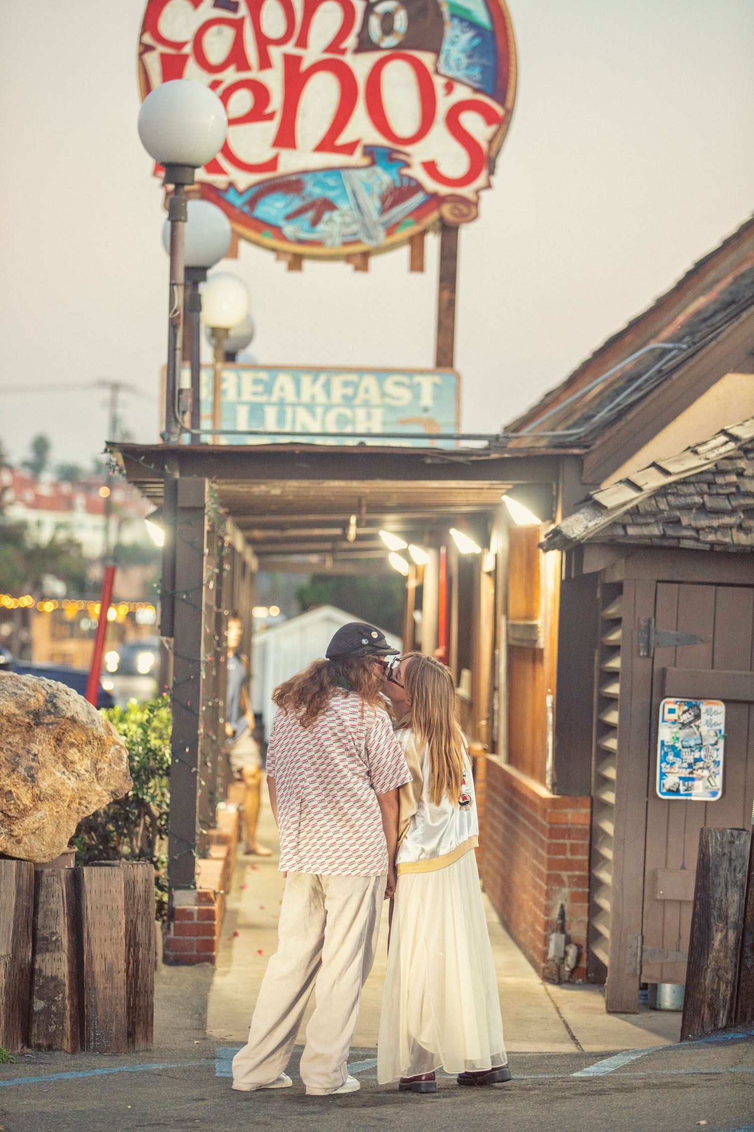 Couple embracing outside Captain Reno's breakfast and lunch restaurant at dusk in a coastal town.