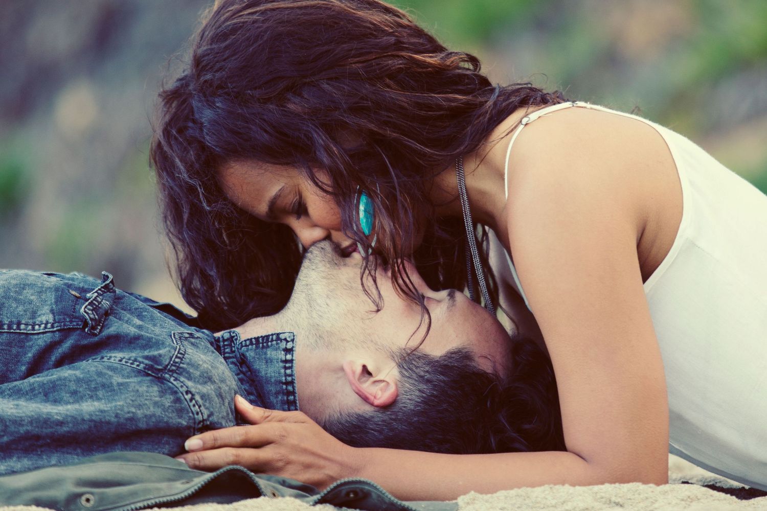 Romantic couple sharing an intimate moment on the beach, woman leaning in to kiss man lying on sand.