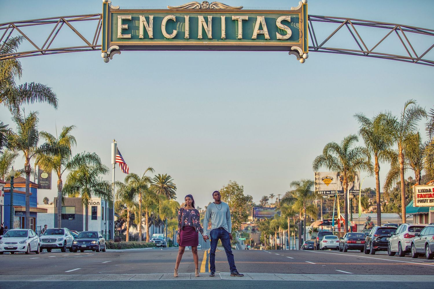 Couple standing under the iconic Encinitas sign on a palm-lined street in Encinitas, California.