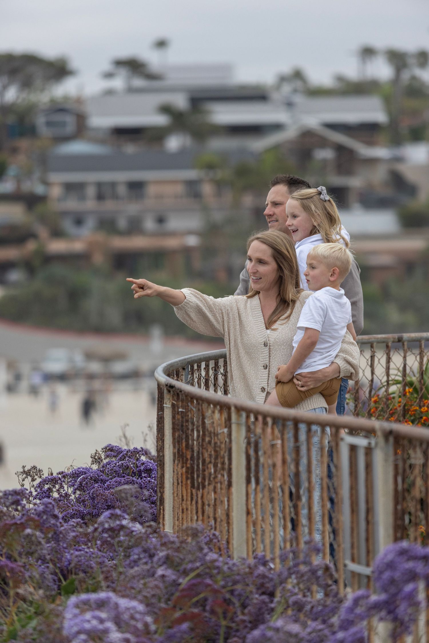 Family of four enjoying a scenic coastal overlook with purple wildflowers, pointing at the ocean view.