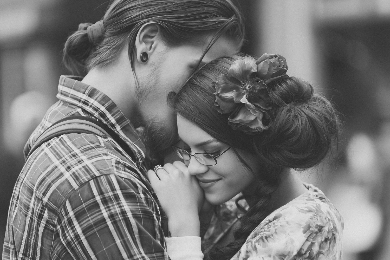 Black and white photo of a romantic couple sharing a tender moment, woman wearing glasses with hair up.