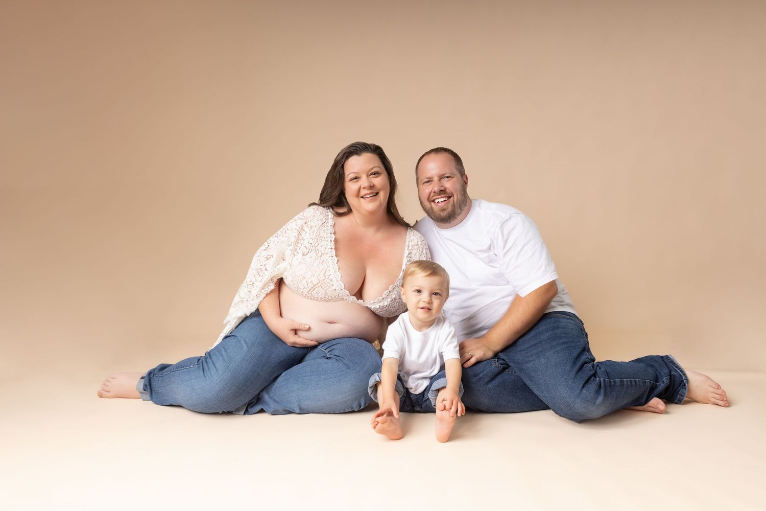 Family members lying on beige backdrop in casual clothing during professional photo session.