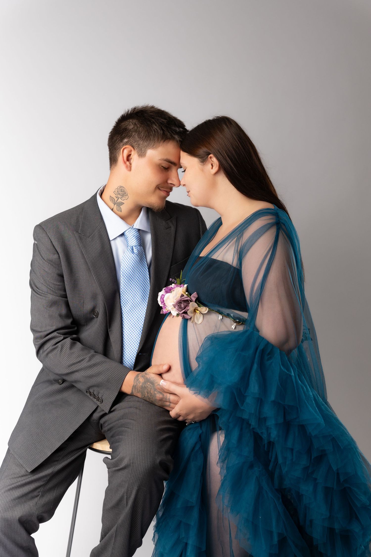 A romantic couple embraces while wearing formal attire with the woman in a flowing navy blue gown and man in grey suit.