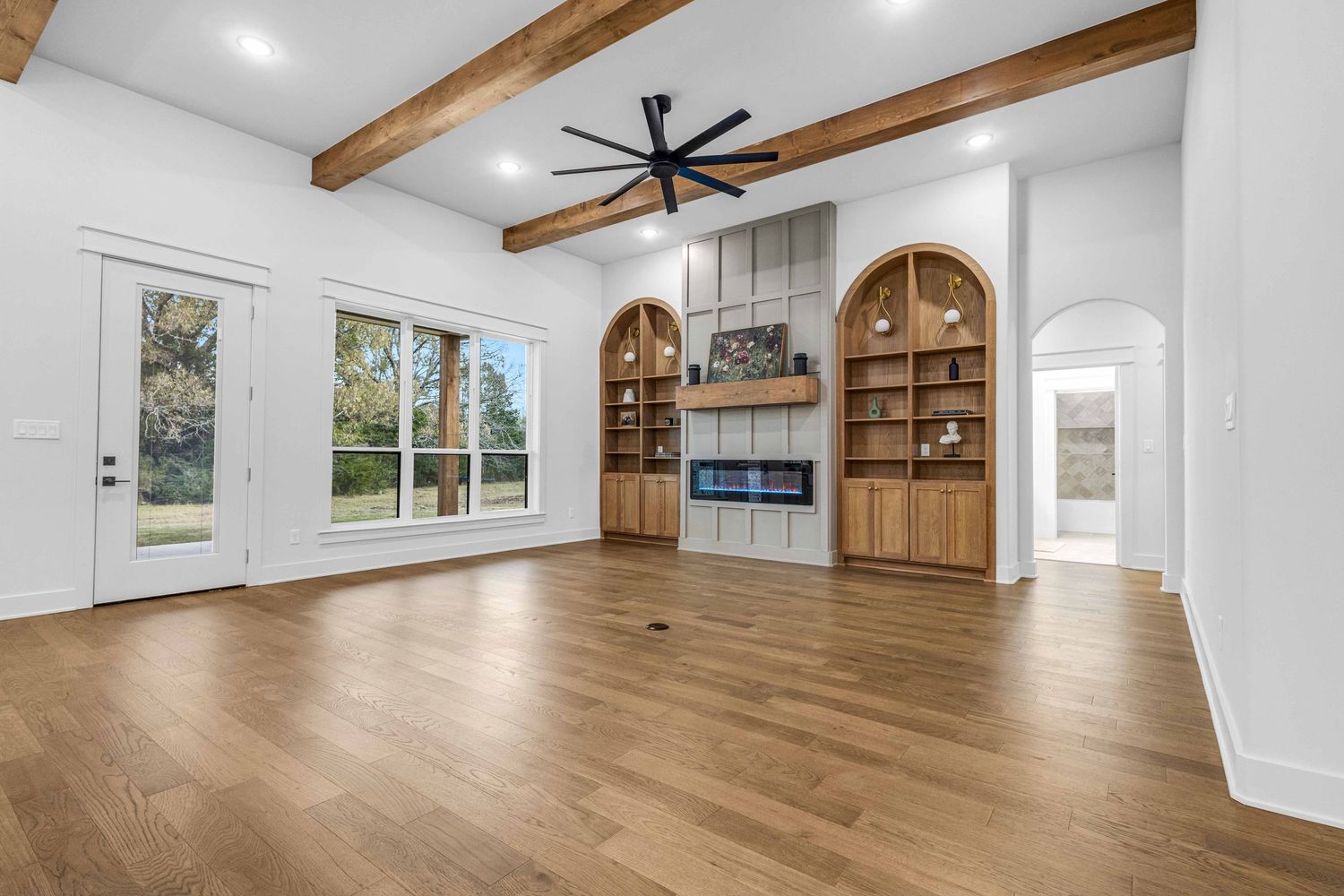 Modern farmhouse style interior with exposed wooden beams, white walls, and wide plank hardwood flooring.