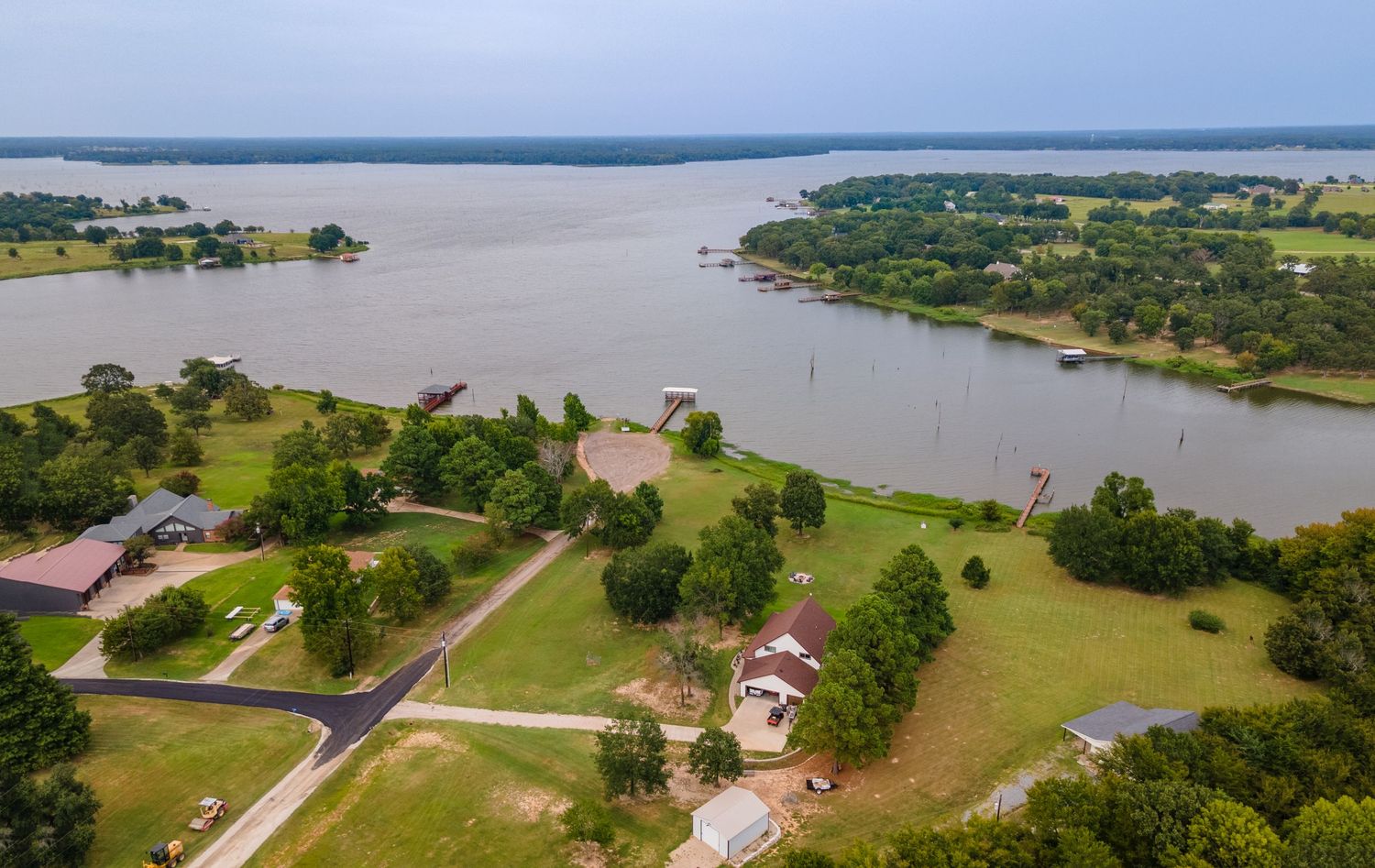 Aerial panoramic view of lakefront homes and properties along a scenic shoreline with green lawns and trees.