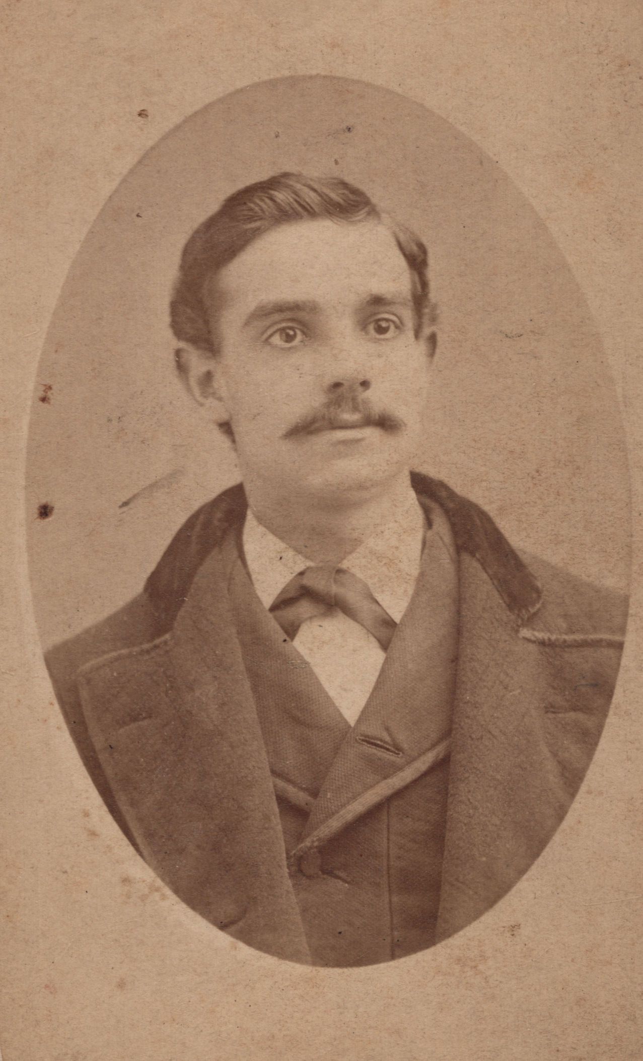Sepia oval portrait of a young Victorian-era man with a mustache wearing a suit jacket, vest, and tie.