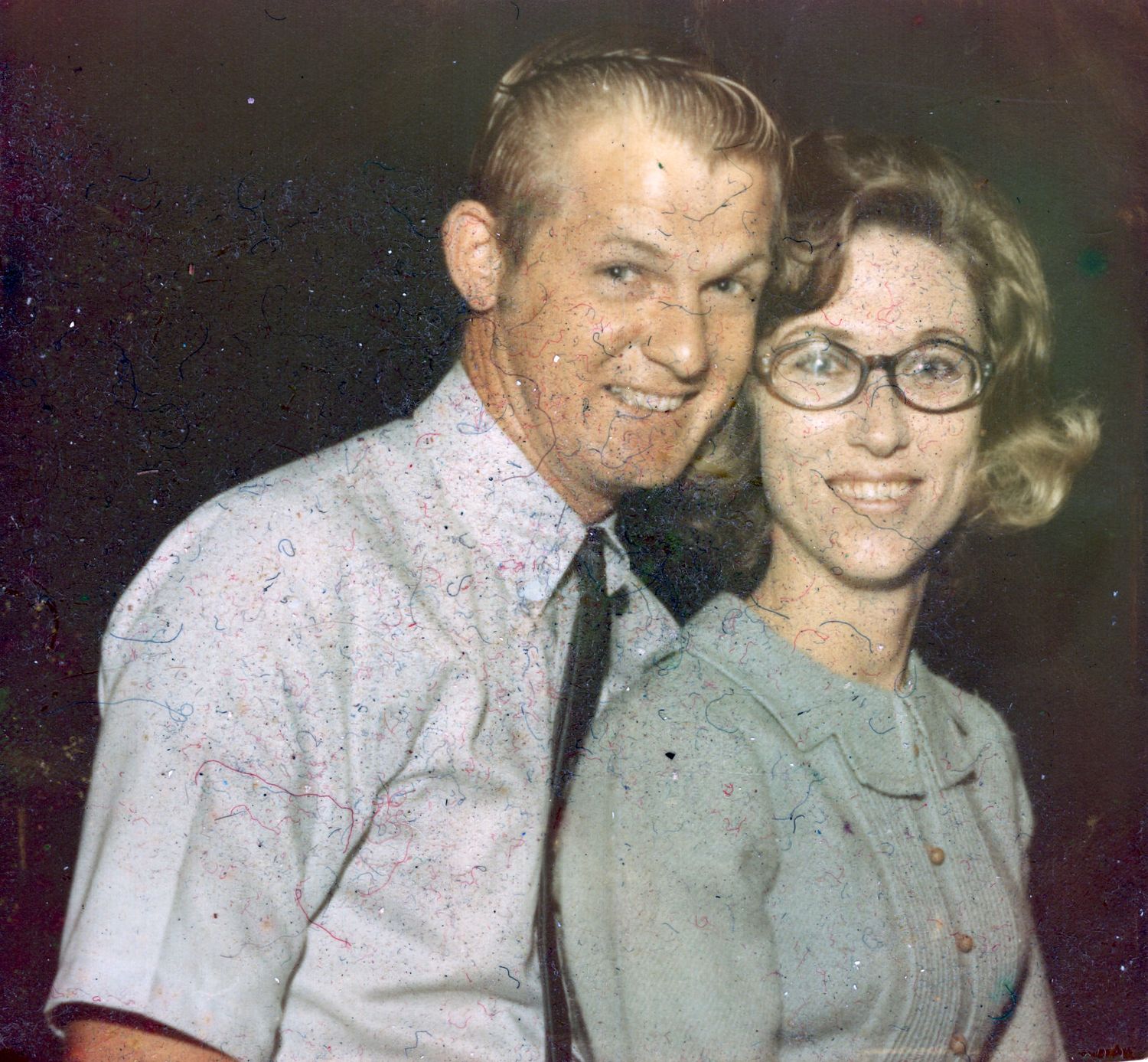 Vintage photo of a smiling couple posing together, man in patterned shirt and woman in glasses.