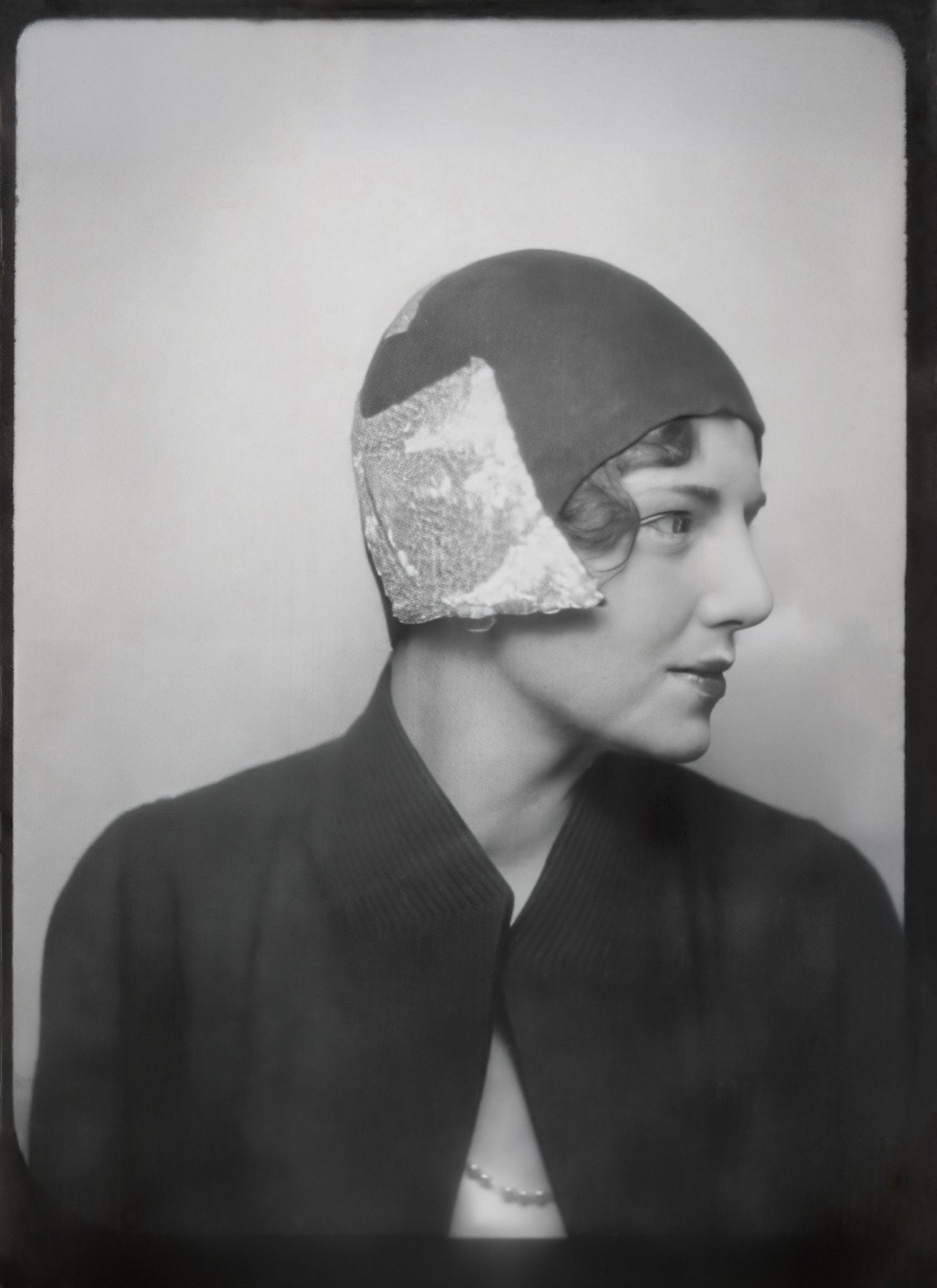 Black and white portrait of a woman in profile wearing a 1930s cloche hat with lace detail and dark jacket.