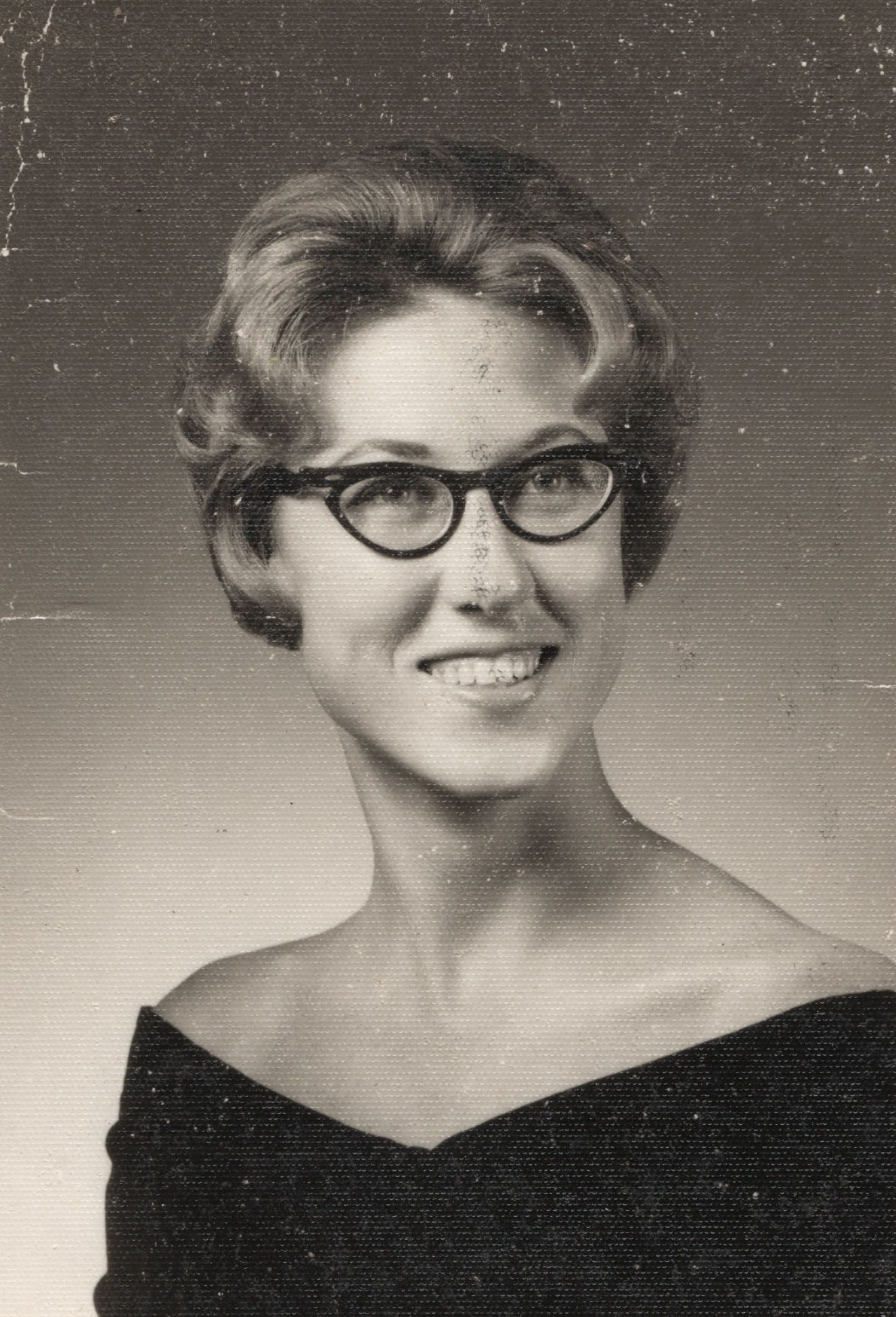 Vintage 1960s black and white portrait of a young woman with cat-eye glasses and bouffant hairstyle.