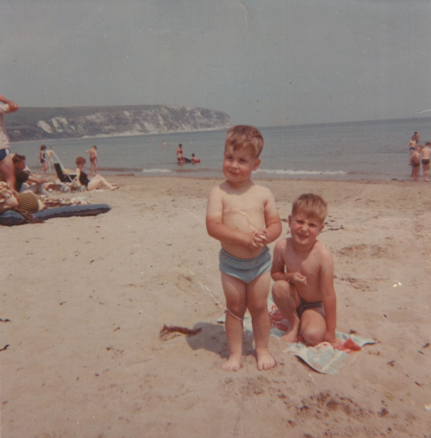 Two young boys posing on a sandy beach with white cliffs and calm ocean in the background on a sunny day.