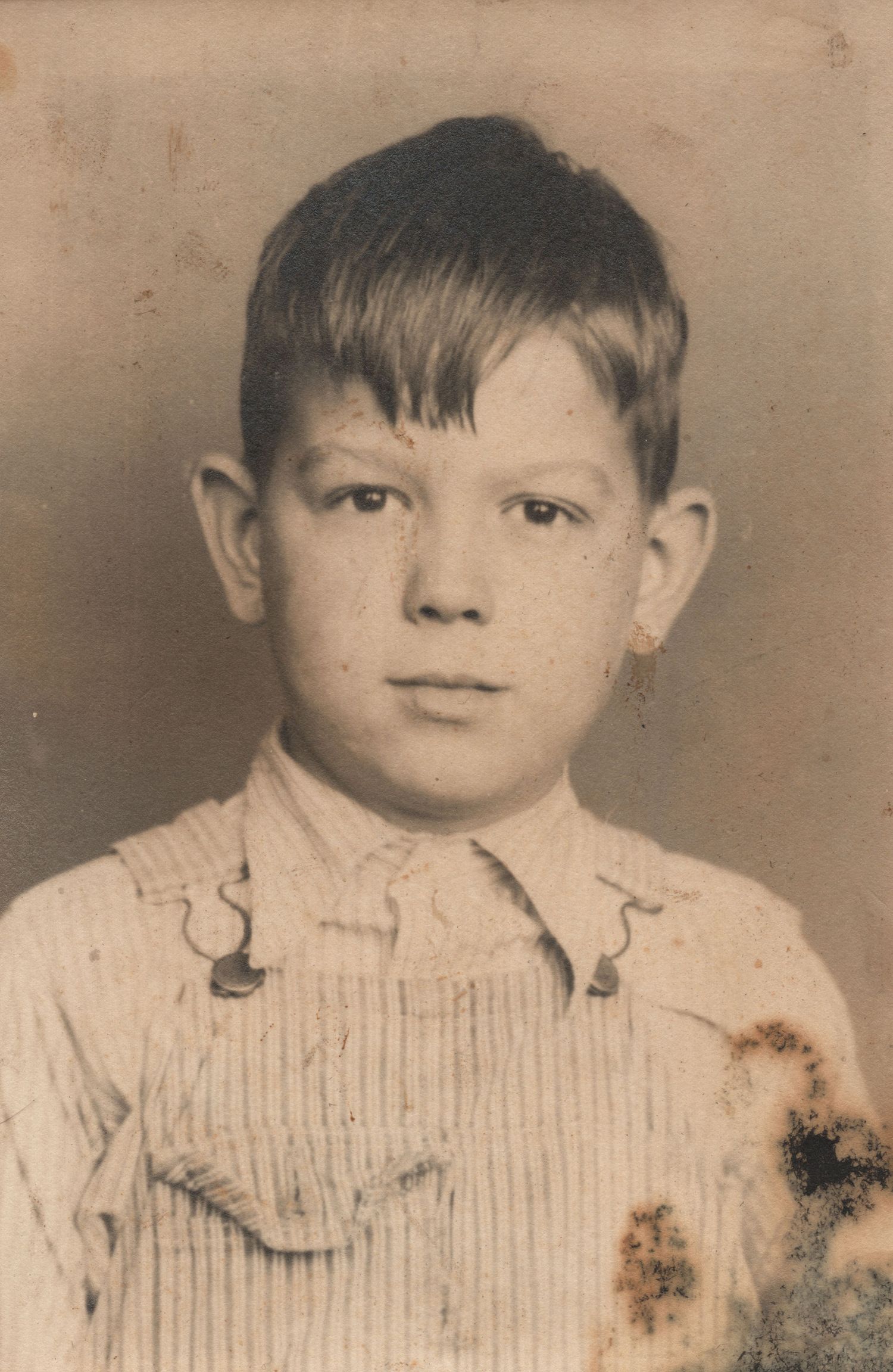 Vintage sepia portrait of a young boy in overalls, old photograph with age spots.