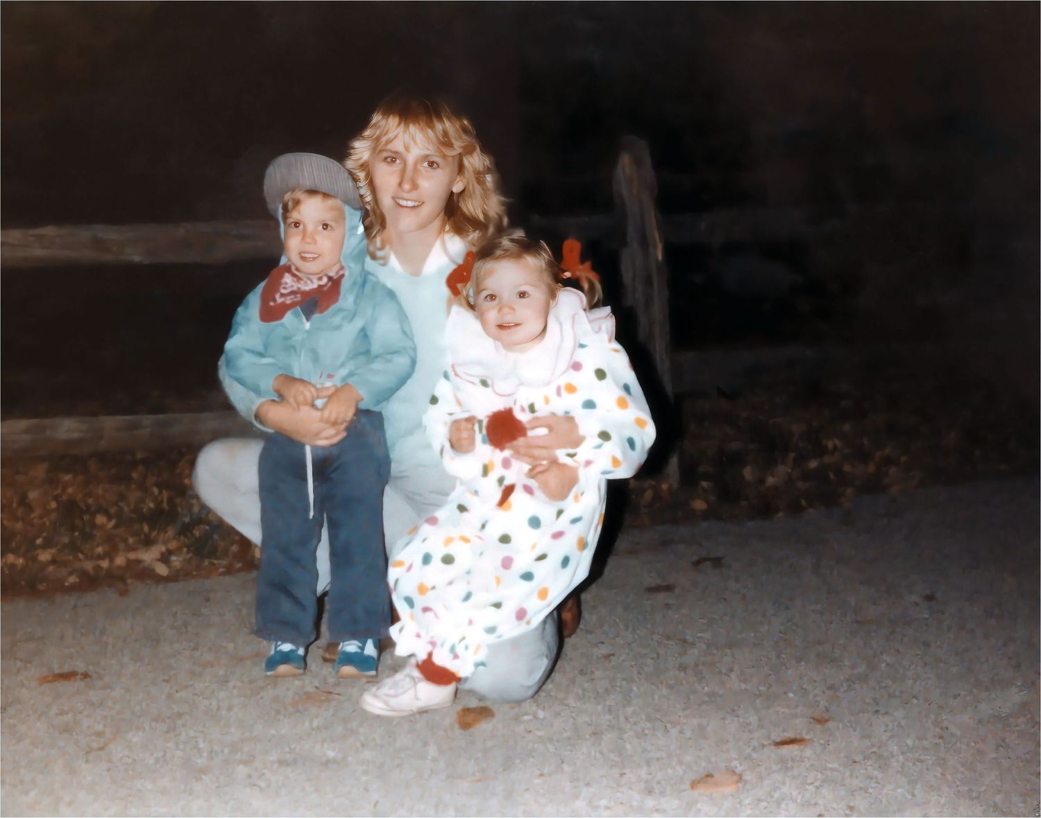 Woman crouching with two young children in Halloween costumes outdoors at night in a vintage 1970s photo.