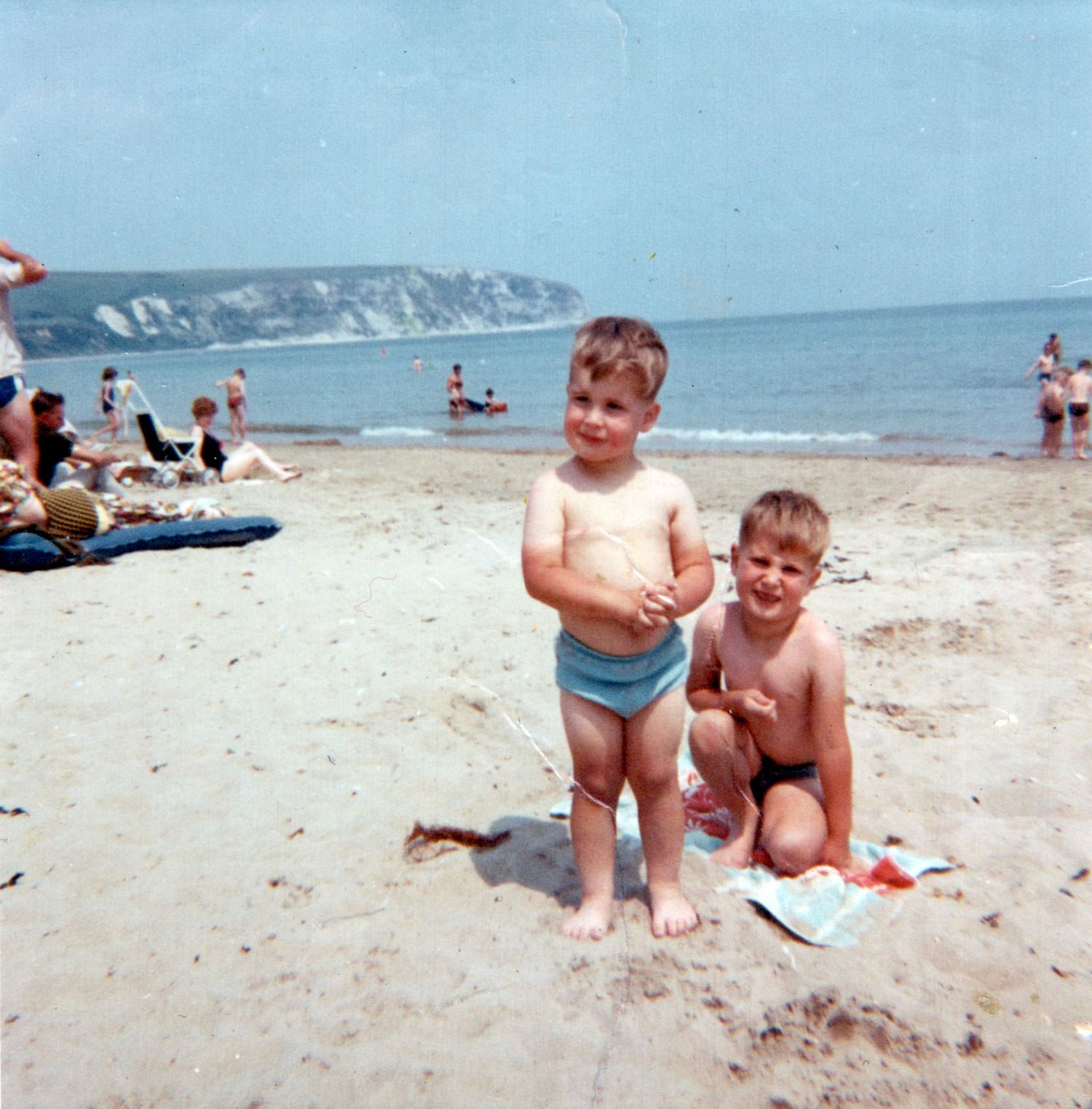 Two young children playing on a sandy beach with white cliffs and calm ocean in the background.