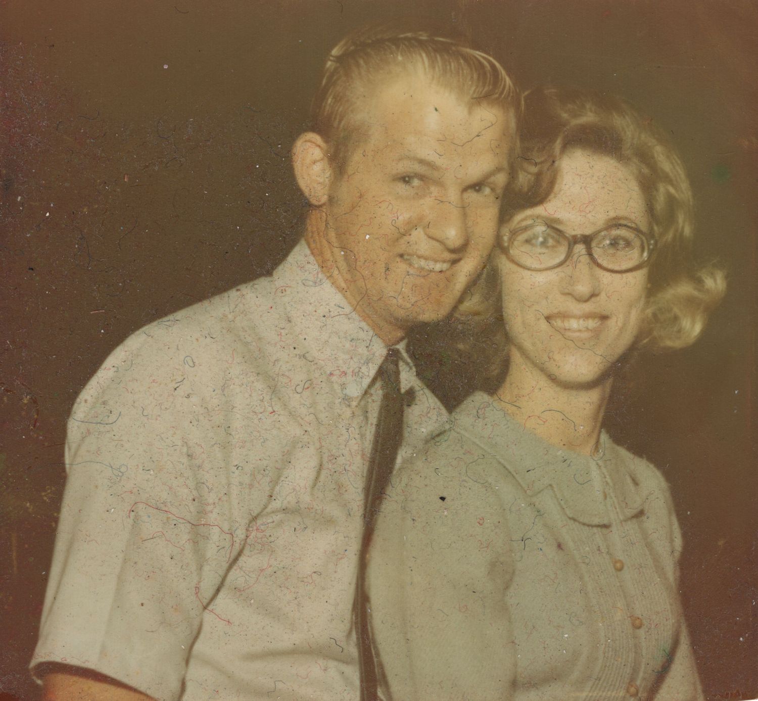 Vintage photo of smiling couple posing together, woman wearing glasses, retro style.