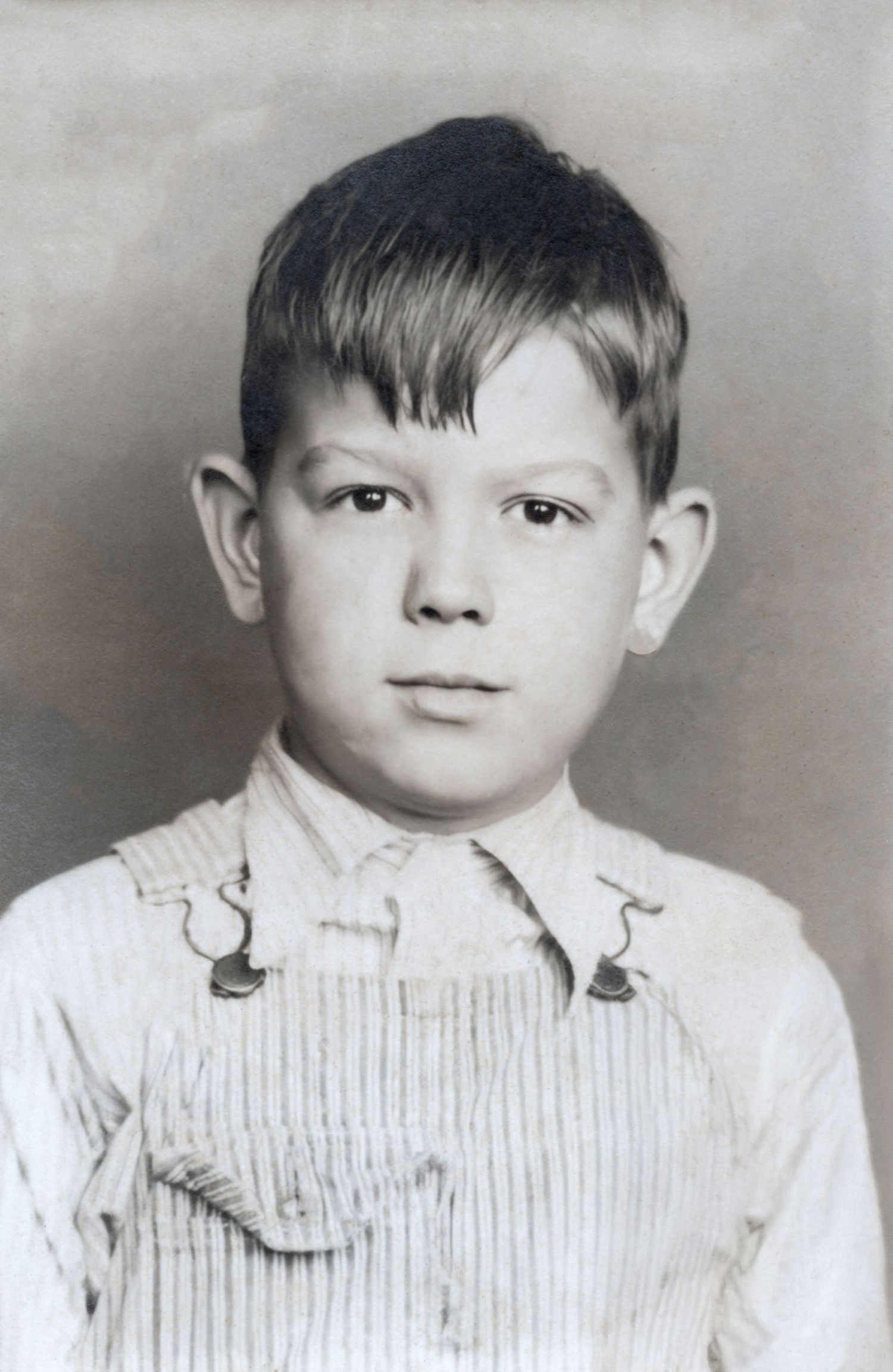 Vintage black and white portrait photo of a young boy wearing overalls and a collared shirt.