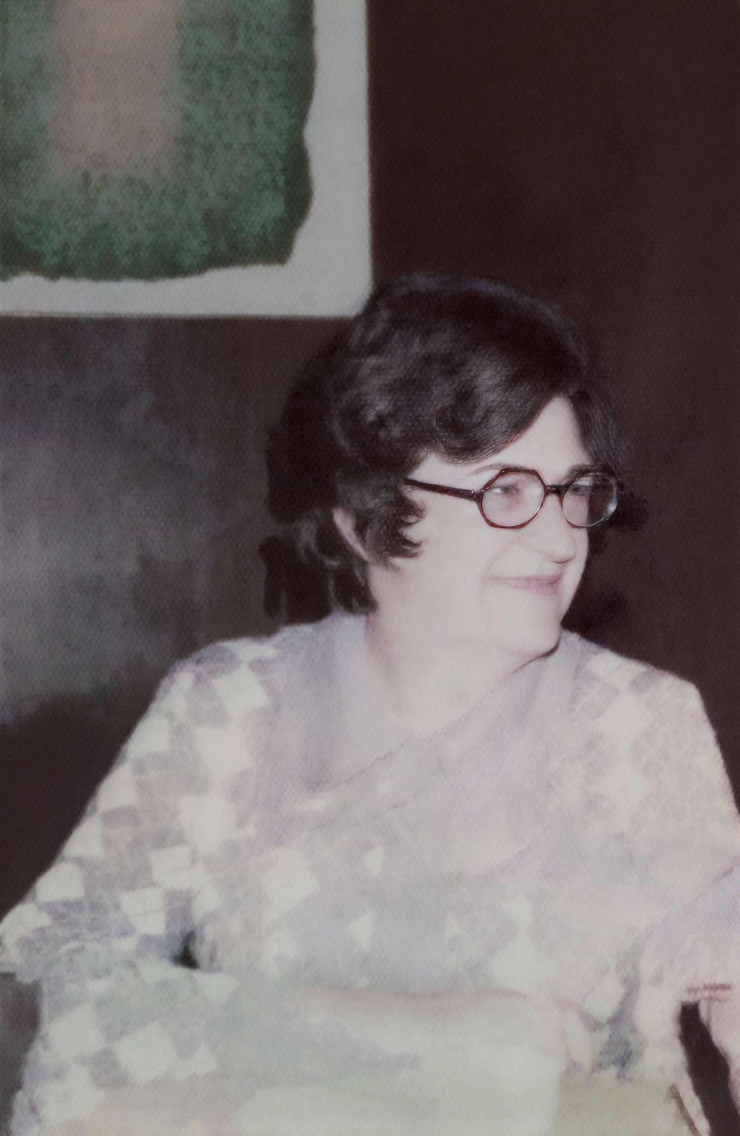 Vintage photo of a young woman with short dark hair wearing round glasses and a patterned blouse, smiling softly.