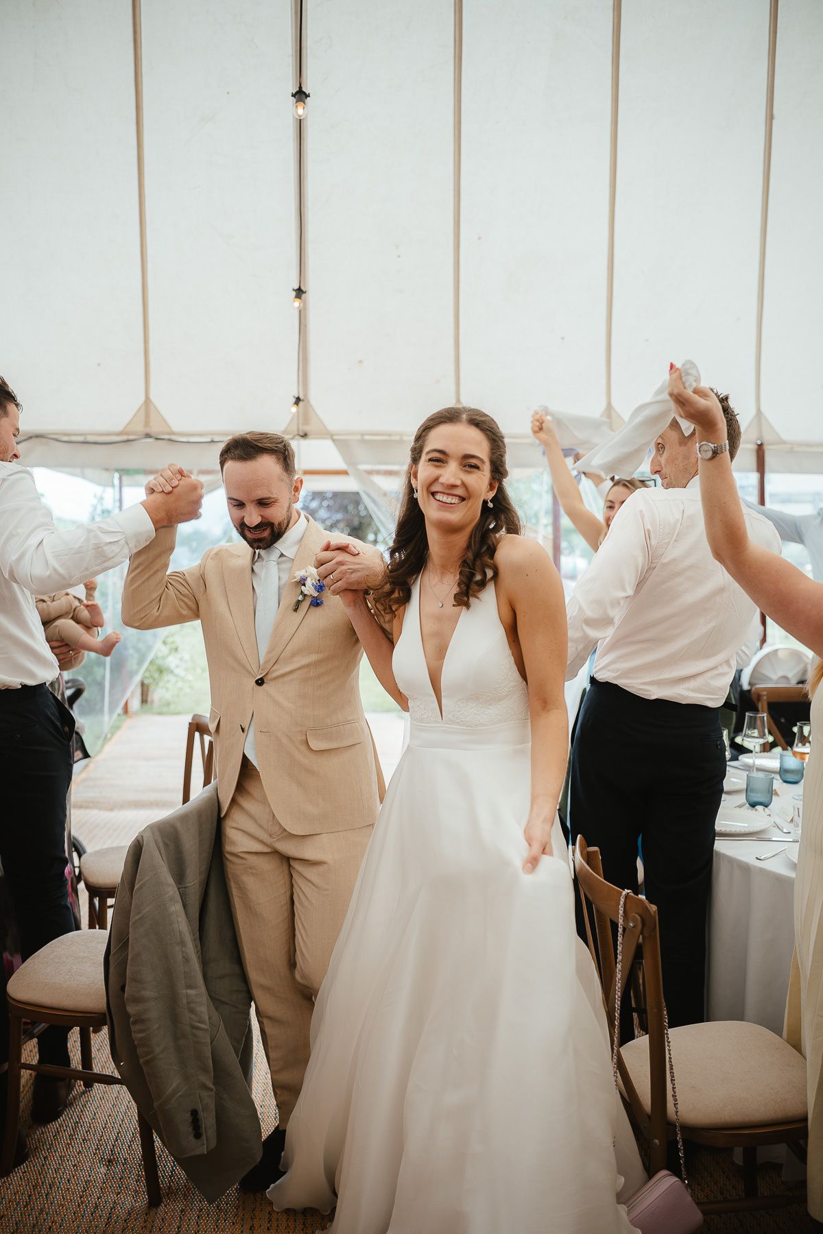 Wedding guests and newlyweds celebrating joyfully under a white tent during the reception.