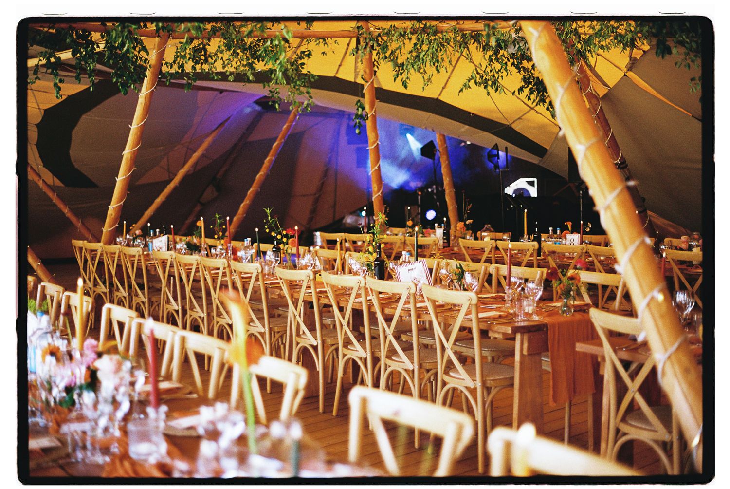 Elegant outdoor wedding reception under a large tent with wooden chairs, long tables, and warm string lights.