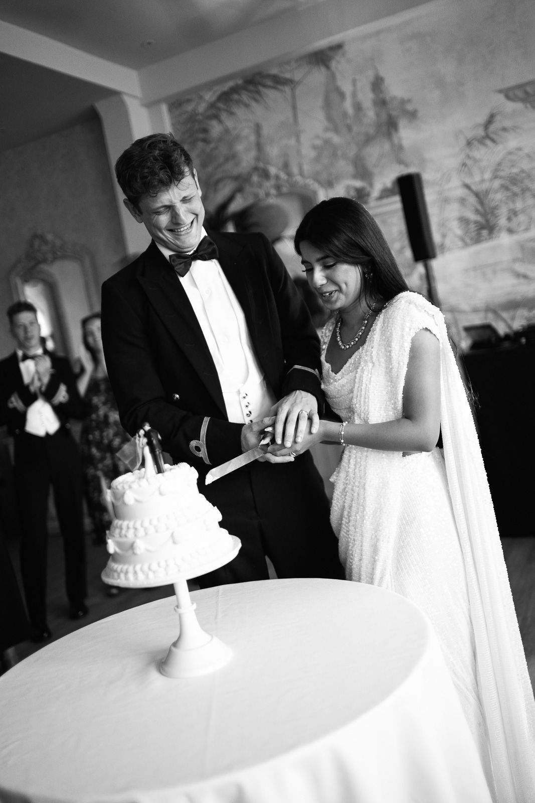 Bride and groom cutting wedding cake together at reception in classic black and white wedding photo.