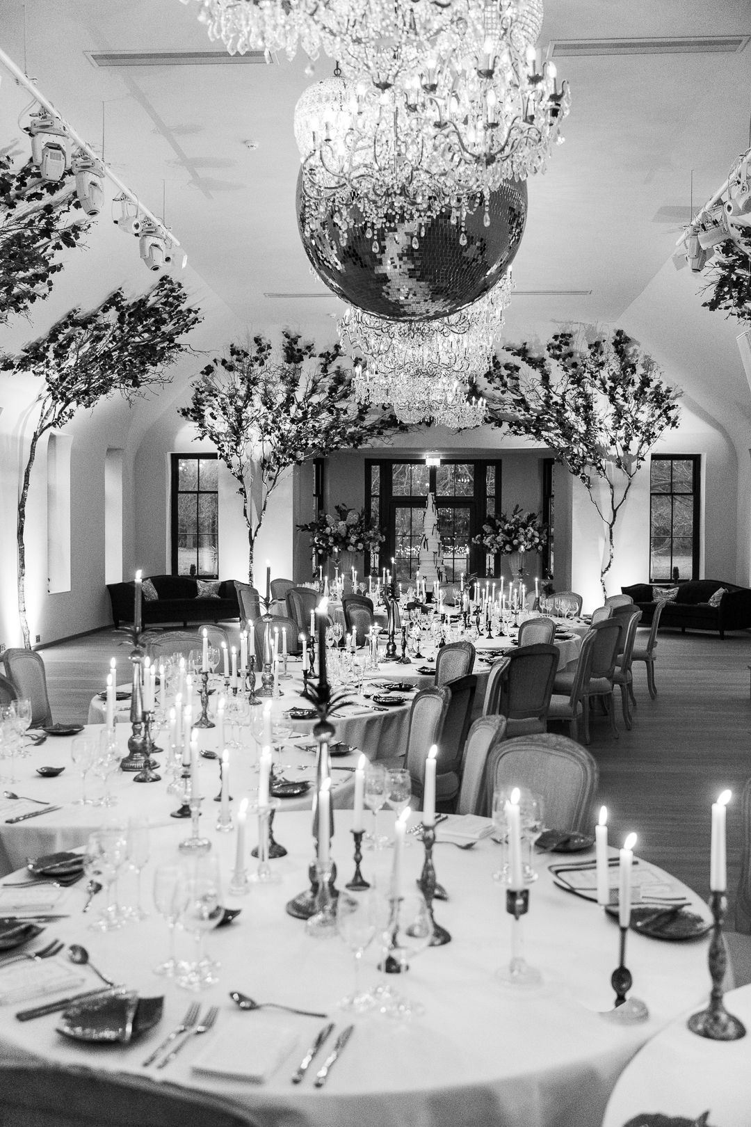 Elegant wedding reception table setting with crystal chandelier, tall floral arrangements and candlesticks in black and white.