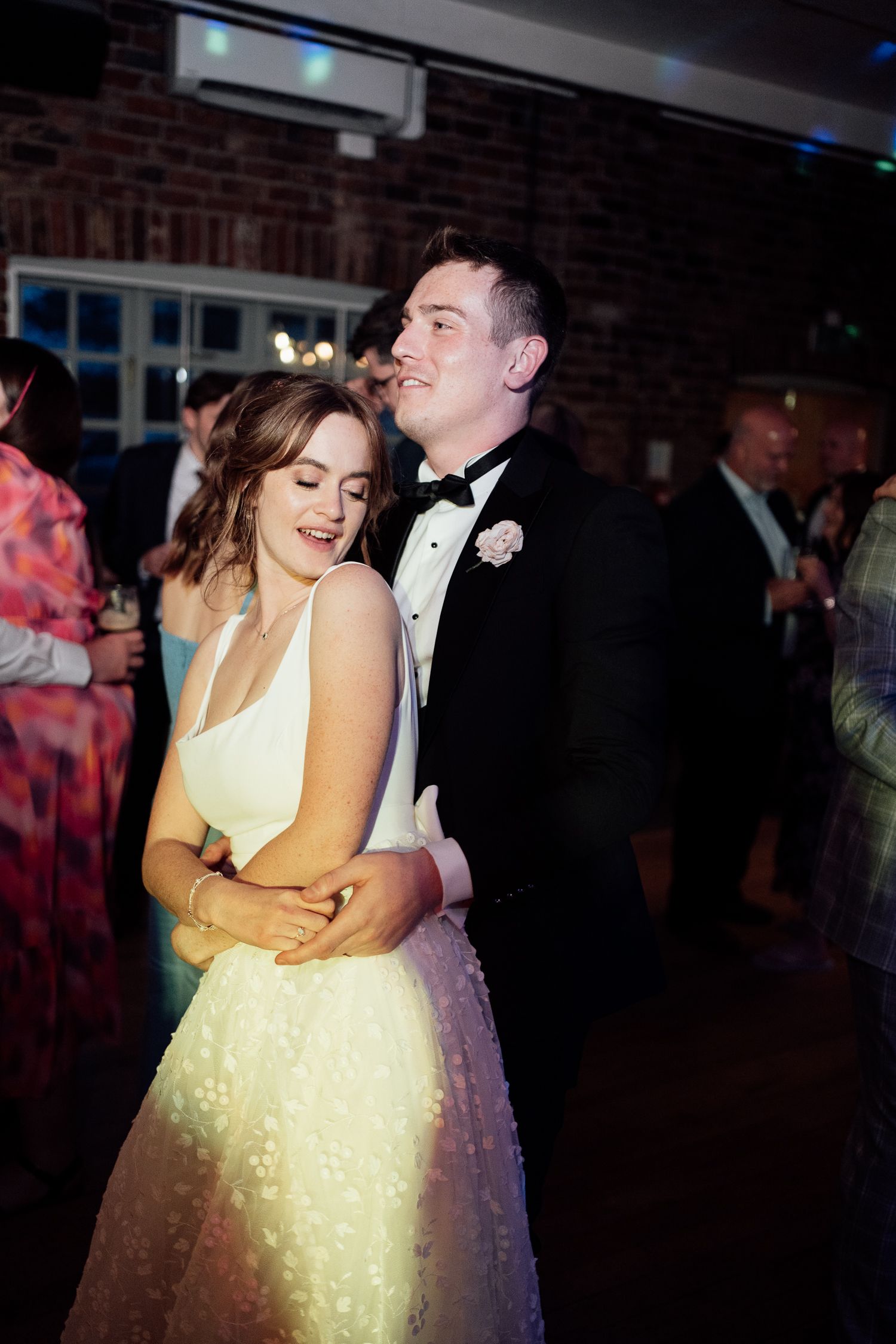 A couple shares a romantic slow dance together at an indoor wedding reception with brick walls.