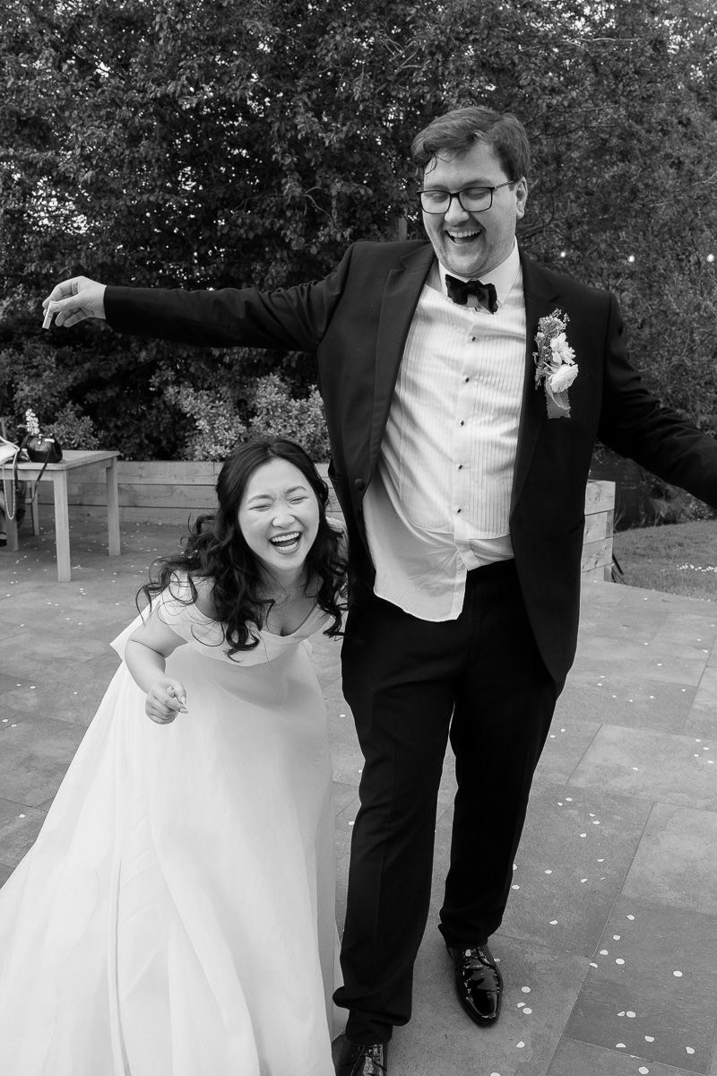 A happy couple in formal wedding attire laughing together outdoors on their special day.