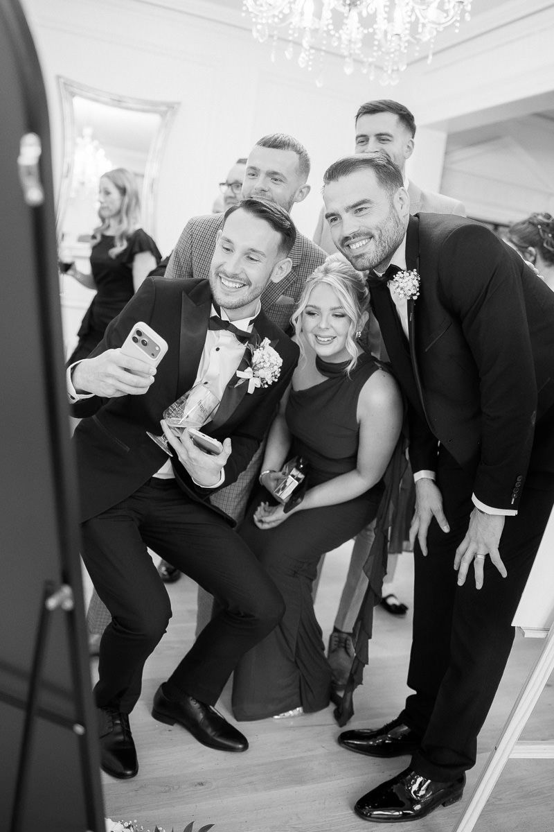 Wedding party members crouch down for playful group photos in formal black attire.