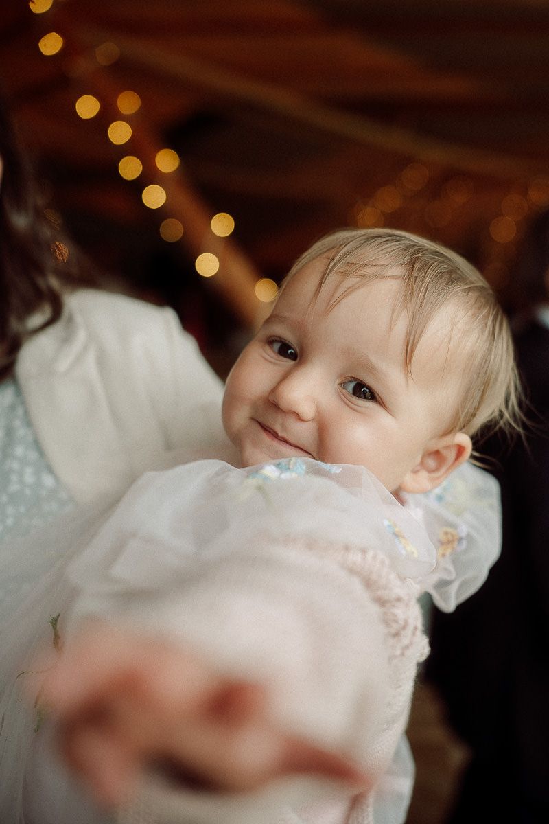 Close-up portrait of a baby in white christening gown with soft bokeh lights in background.