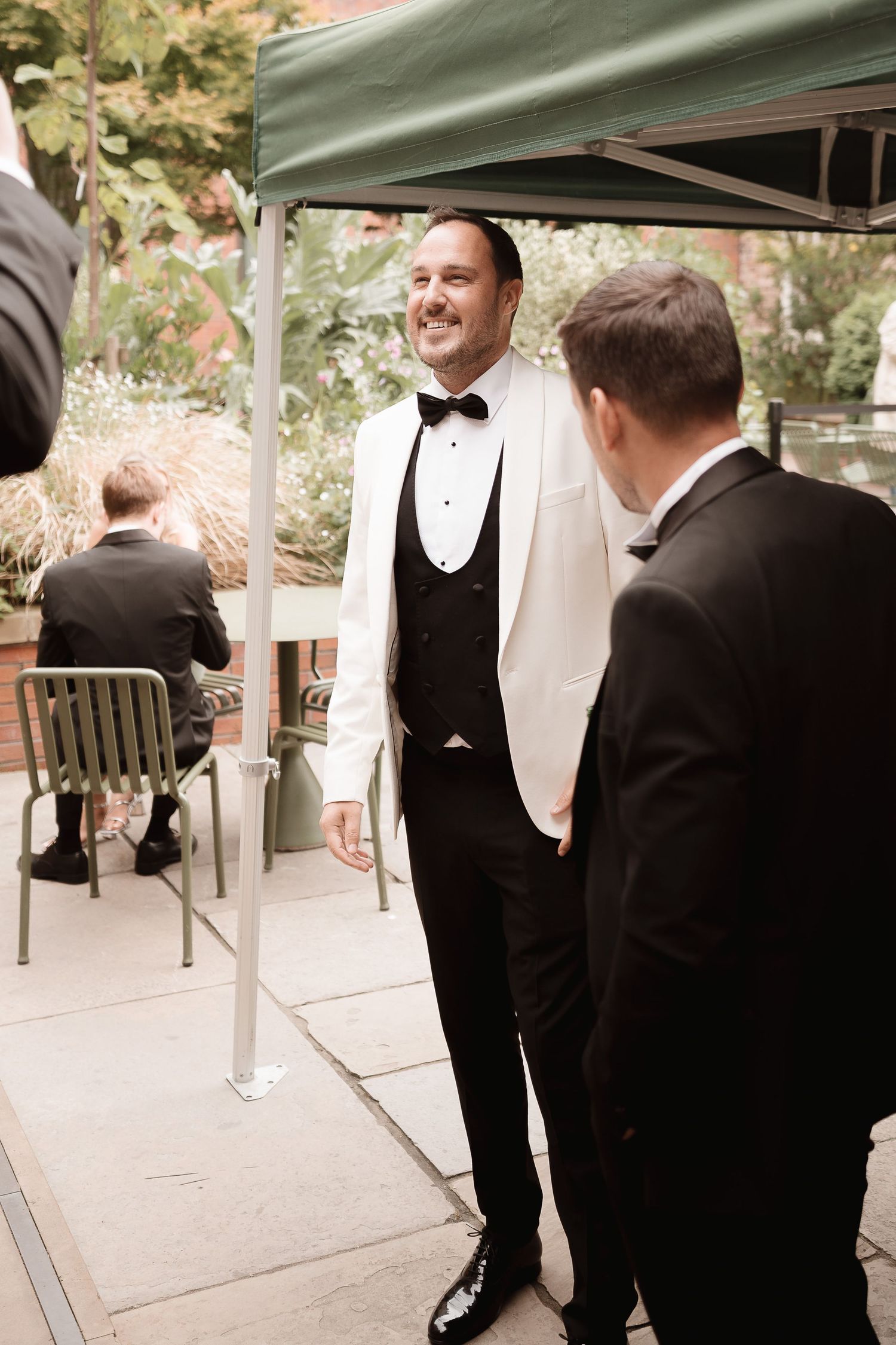 Elegantly dressed guests in formal black and white tuxedos gather under a canopy at an outdoor event.