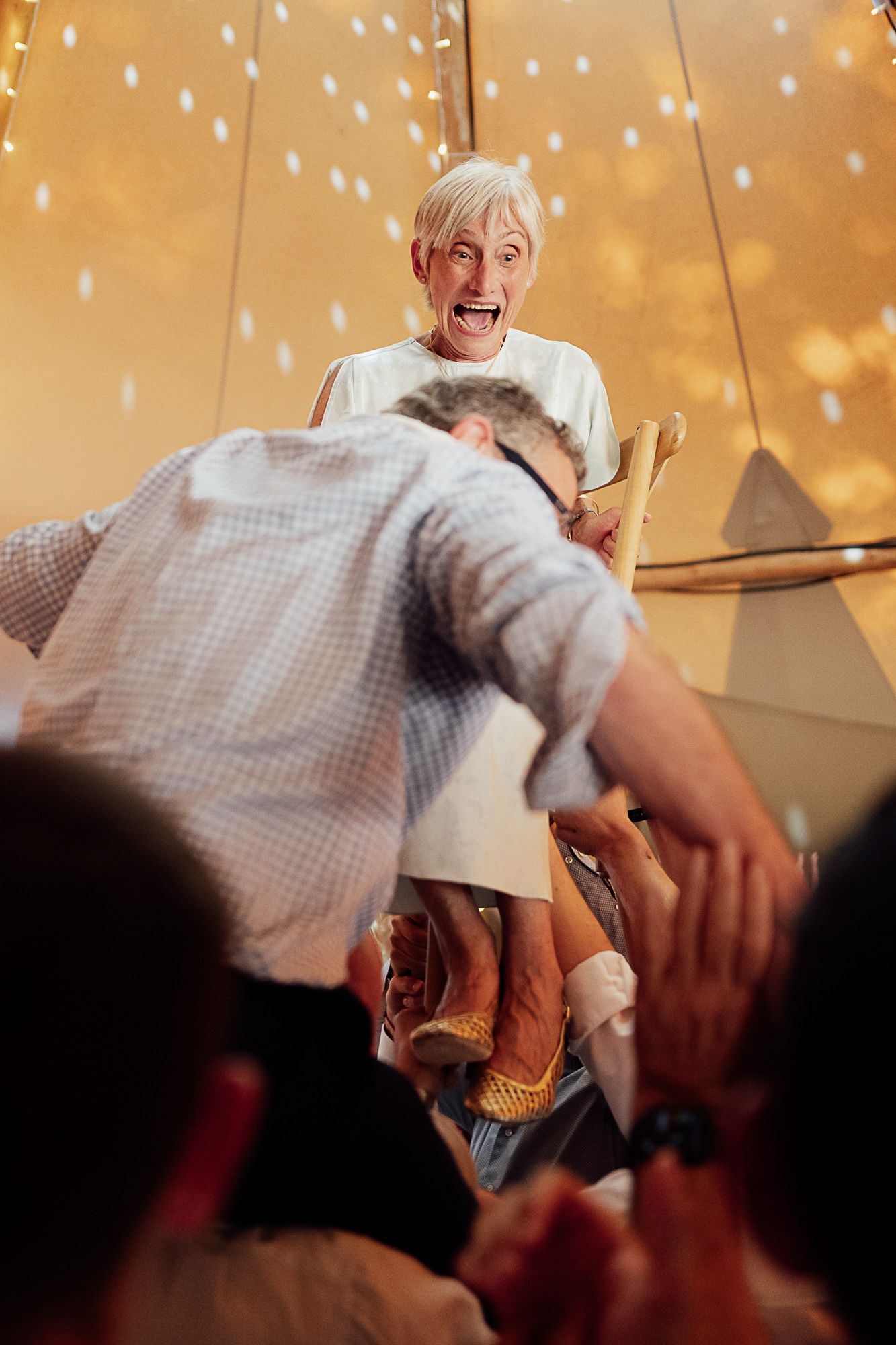 Excited elderly woman laughing as man bows before her at lively indoor celebration event.