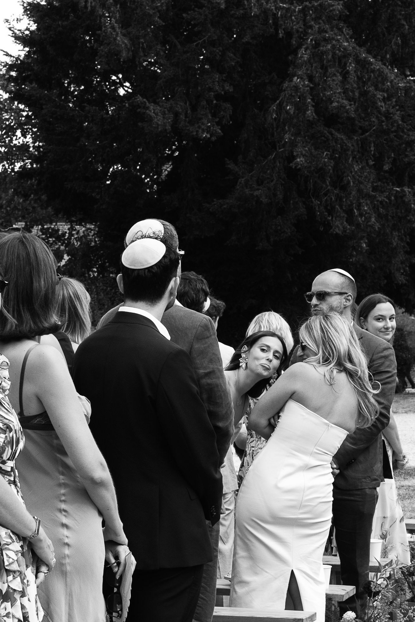 Black and white photo of wedding guests mingling outdoors, bride in white dress receiving congratulations.