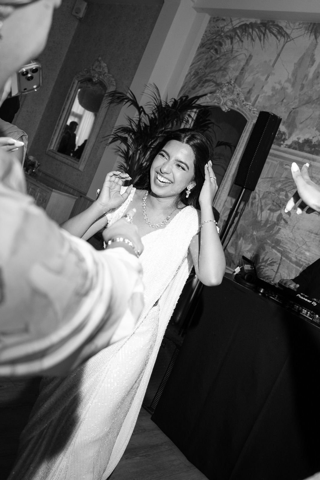 Bride laughs joyfully wearing feathered headpiece while dancing at wedding reception.