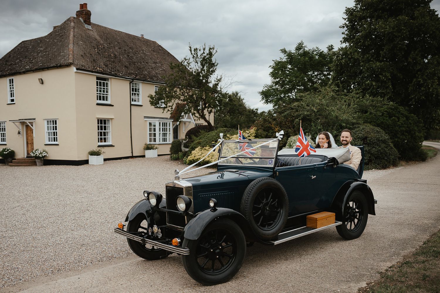 Vintage black convertible car parked in front of traditional thatched roof English countryside house.