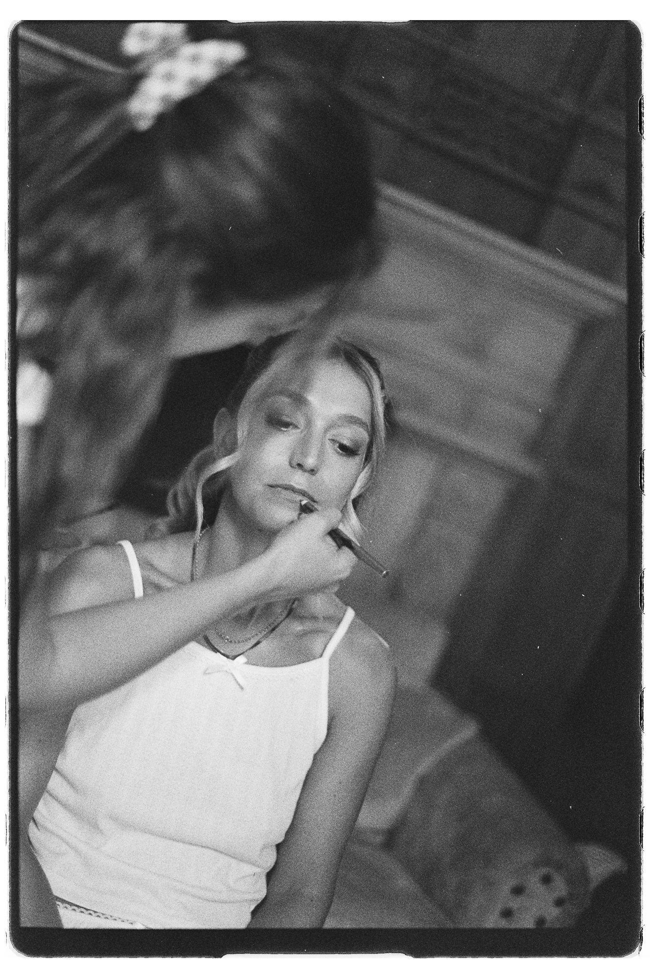 Black and white photo of a woman having makeup applied to her lips by another person.