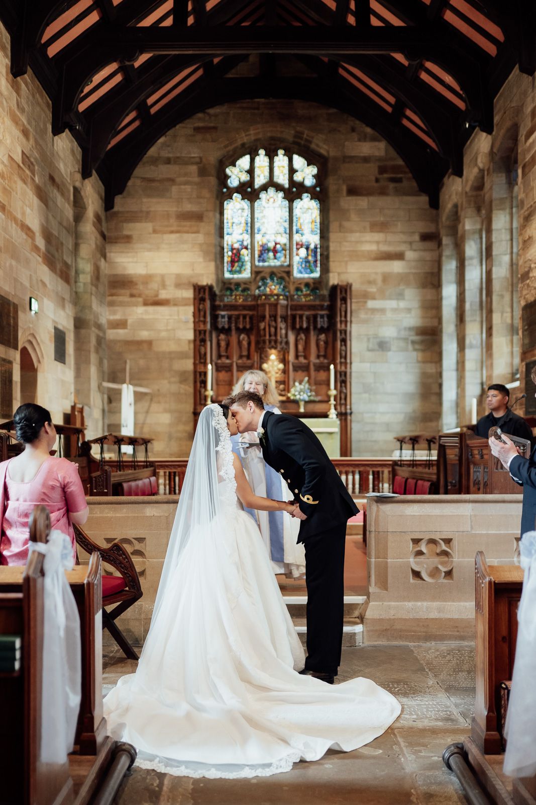 Bride and groom share an intimate moment at the altar inside a stunning stone church with stained glass windows.