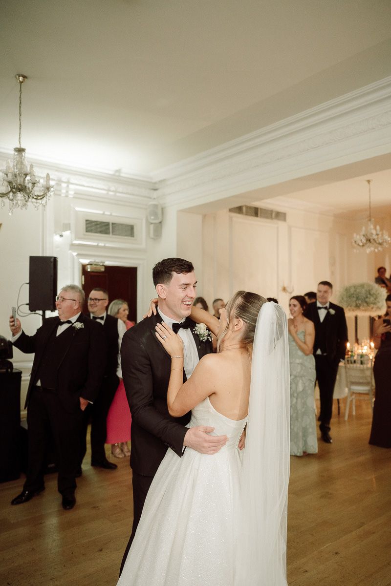 A couple shares their first dance at an elegant wedding reception with chandeliers and guests looking on at West Tower venue.