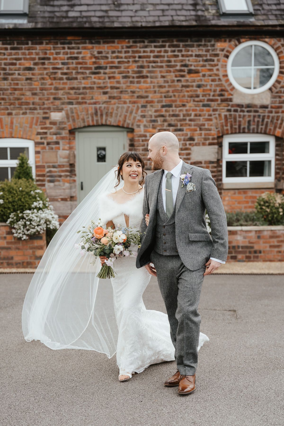 Two newlyweds share a joyful moment together outside a rustic brick building on their wedding day.