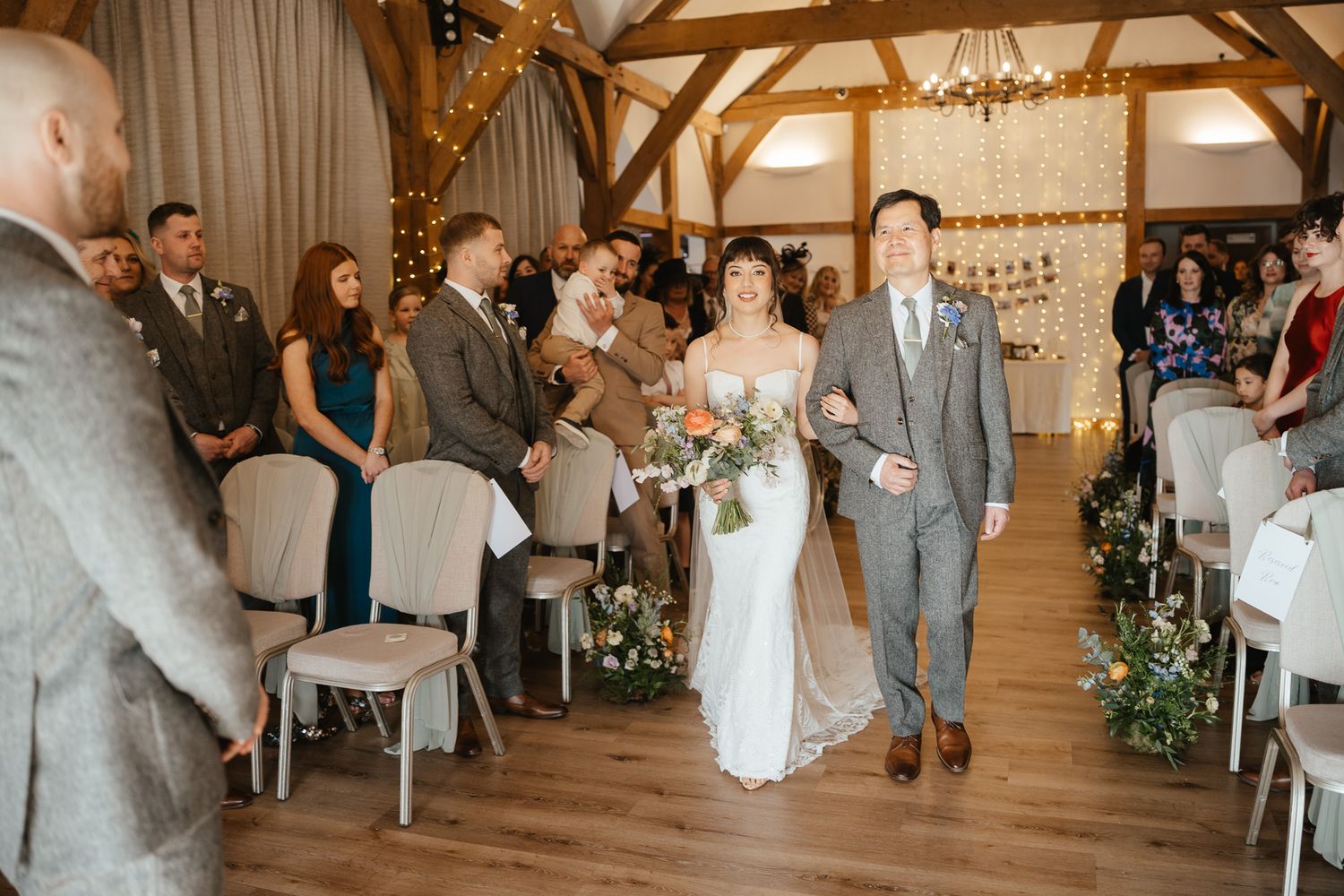 People dance and celebrate at a rustic barn wedding reception with exposed wooden beams and string lights.
