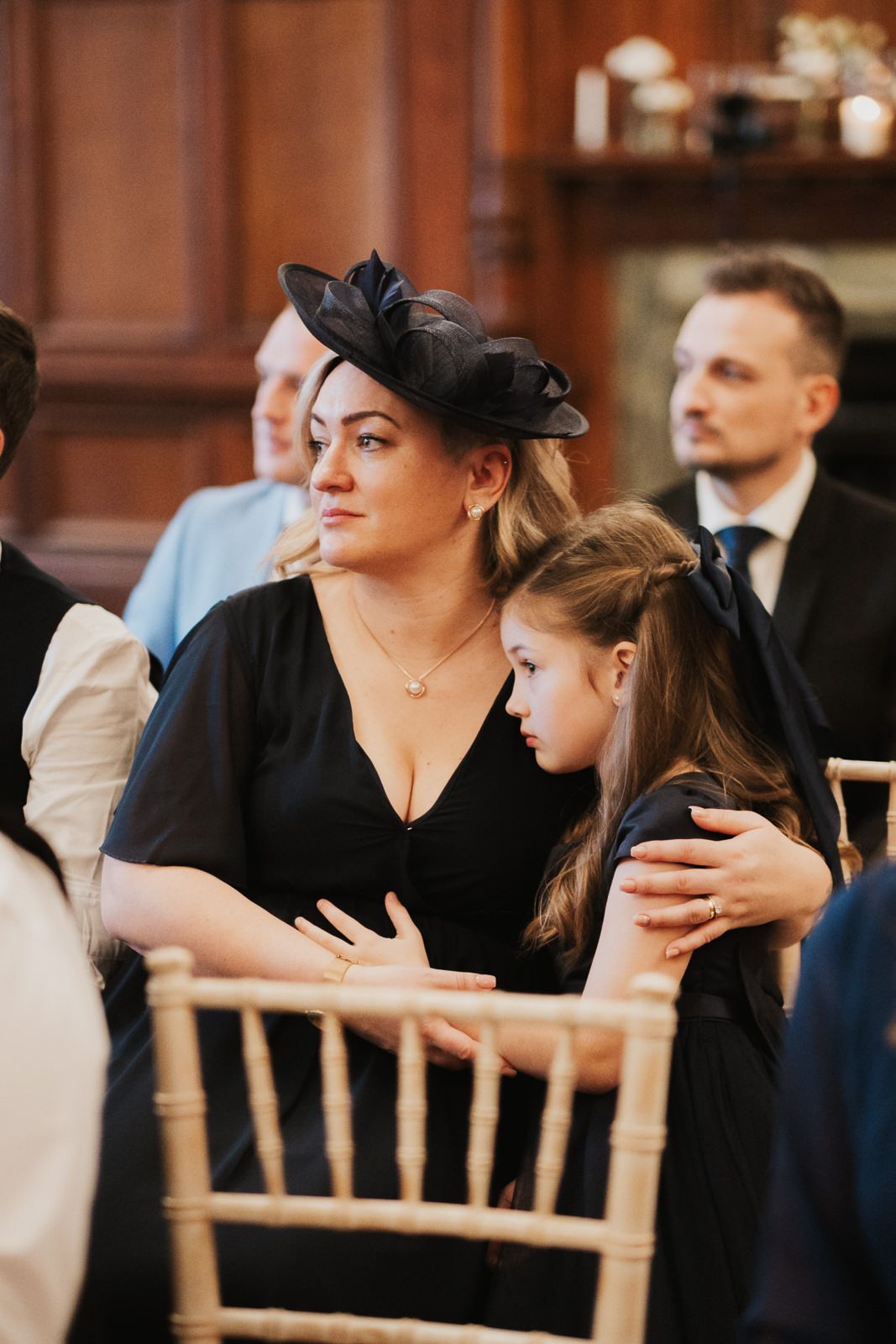 Wedding guests seated in formal attire on chiavari chairs during indoor ceremony.