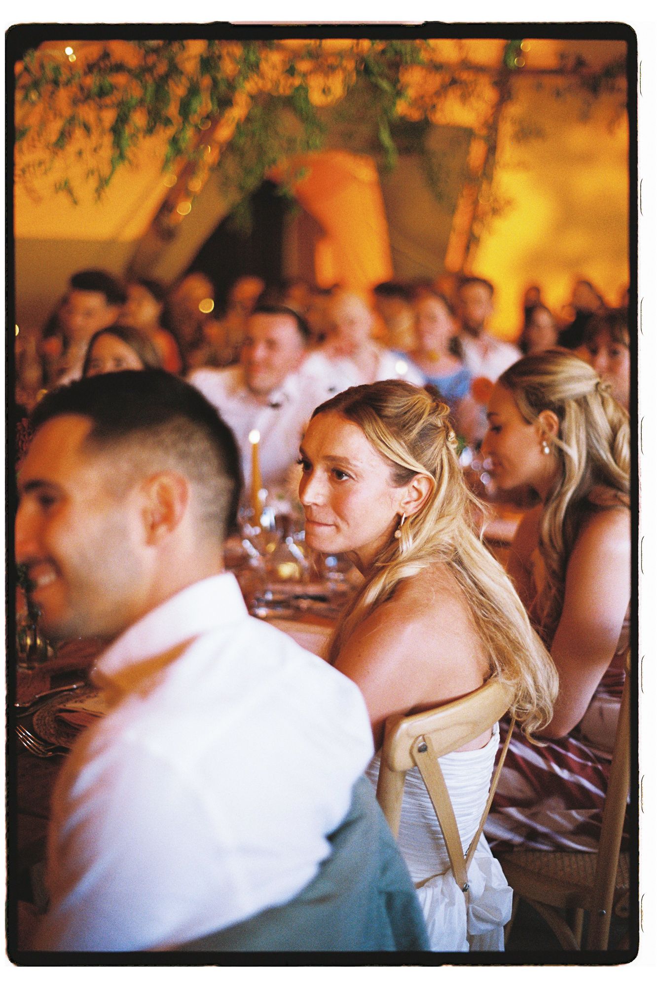 Guests seated at an elegant outdoor wedding reception, smiling woman in white dress enjoying the celebration.