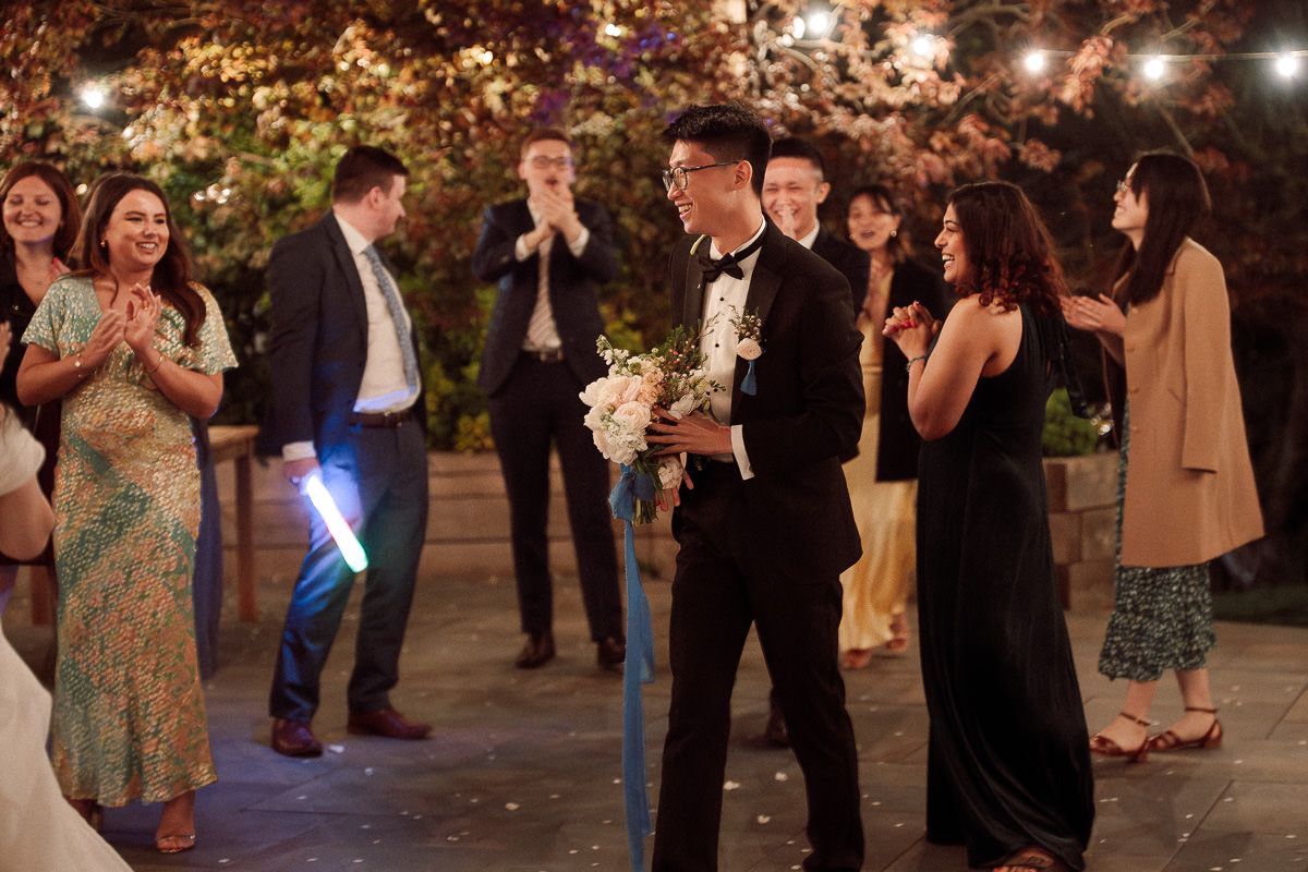 People dancing together at a dimly lit evening celebration with decorative lights and trees in the background.