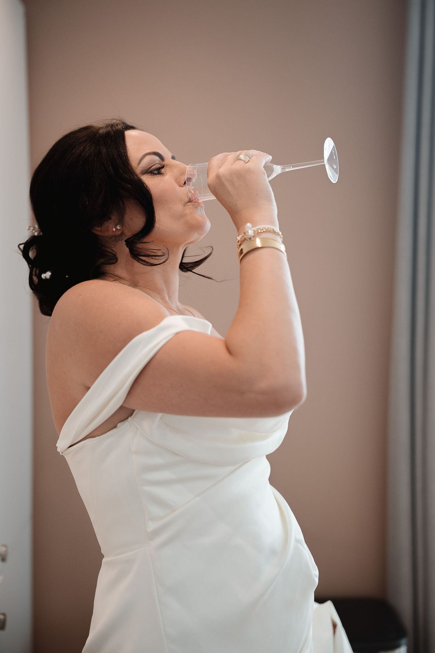 Someone in an elegant white wedding dress takes a sip from a champagne glass during a celebratory moment.