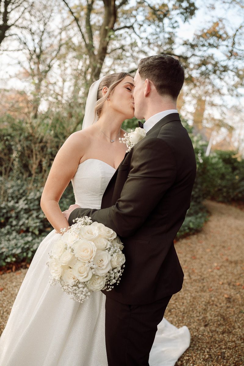 A romantic wedding couple shares intimate moments in a wooded outdoor setting with autumn leaves on the ground.