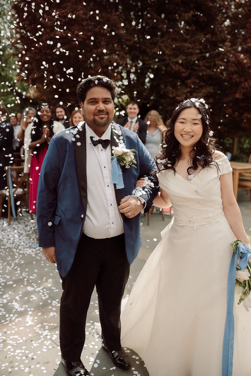 Wedding celebration with confetti falling as guests celebrate outdoors on a sunny day.
