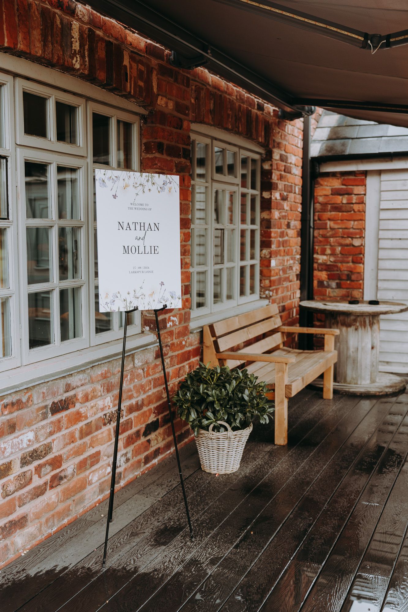 A rustic wooden bench sits on a porch against red brick wall with vintage windows and signage.