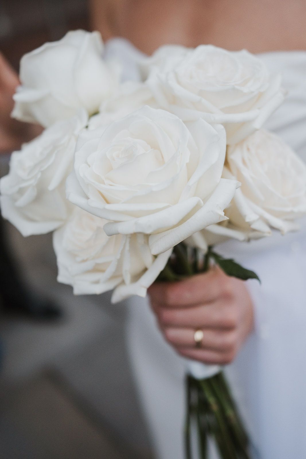 A bouquet of pure white roses held by someone wearing white with an engagement ring visible.