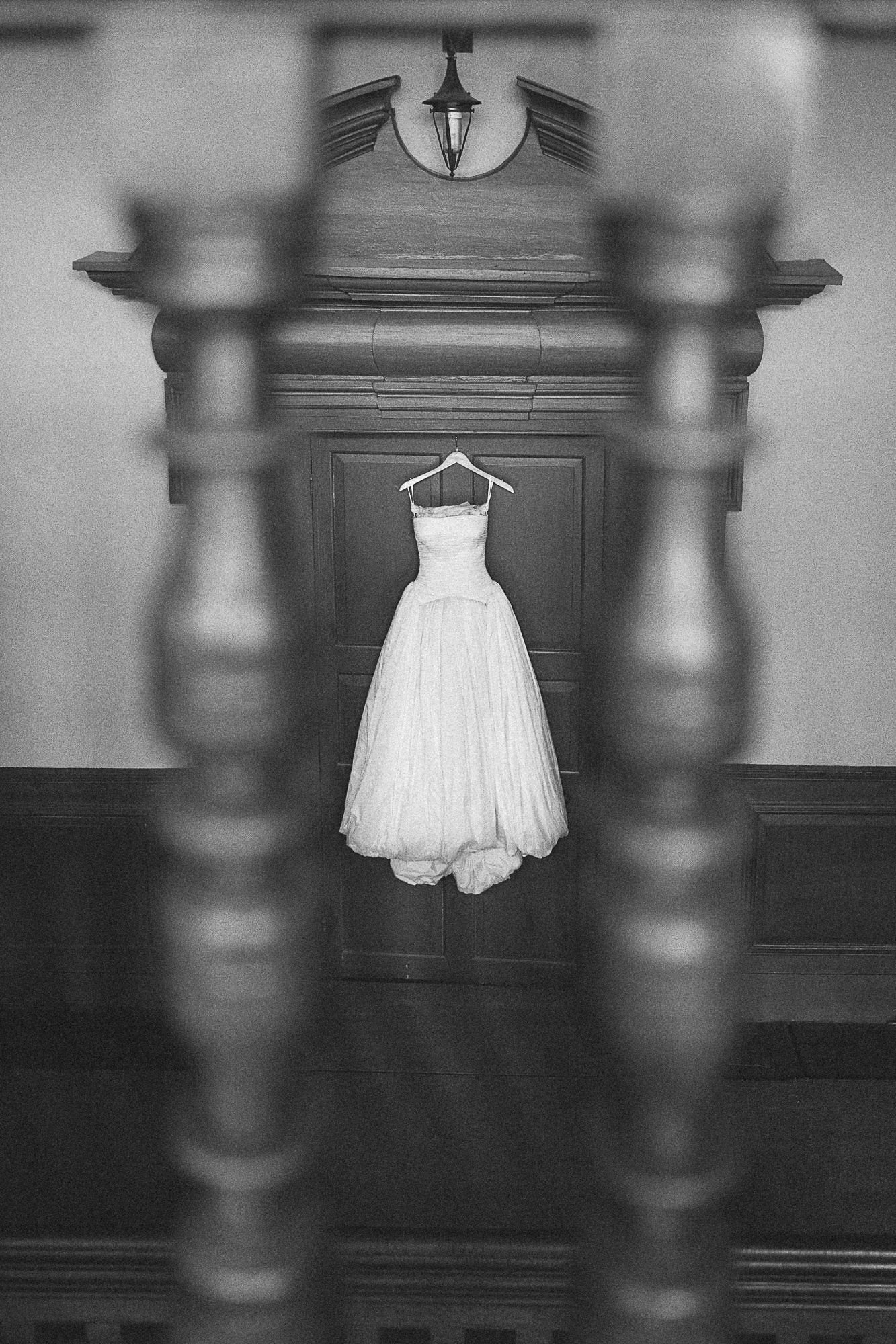 Black and white photo of a strapless ball gown wedding dress hanging on a hanger between staircase balusters.