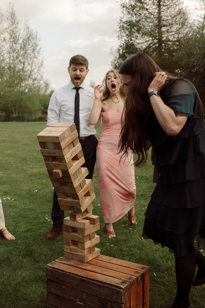 Dramatic moment as giant Jenga tower falls during outdoor party on grass.