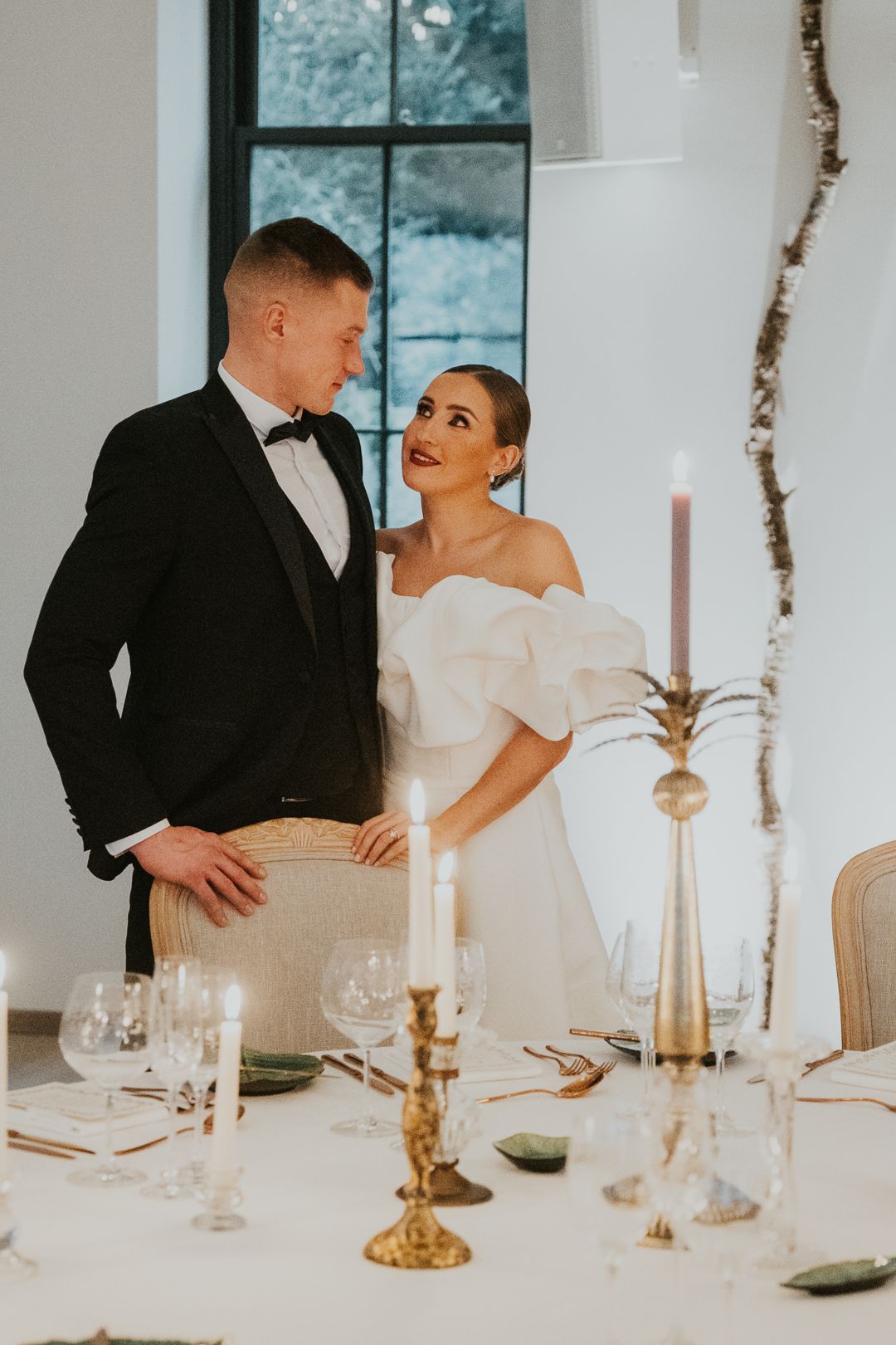Elegant couple shares romantic moment at formal dinner table with candlesticks and fine glassware.